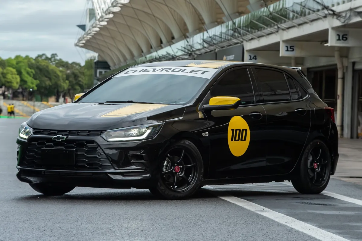 Chevrolet Onix Track Day com faixas amarelas e número 100 na porta em pista de corrida