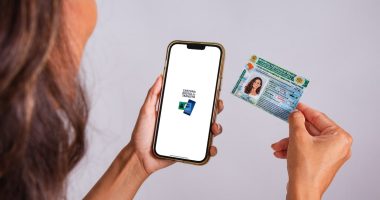 Mão segurando uma CNH brasileira com fundo desfocado de uma rua em Portugal