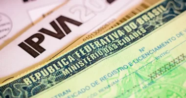 Pessoa analisando tela de computador com site de pagamento de impostos enquanto segura cartão e celular