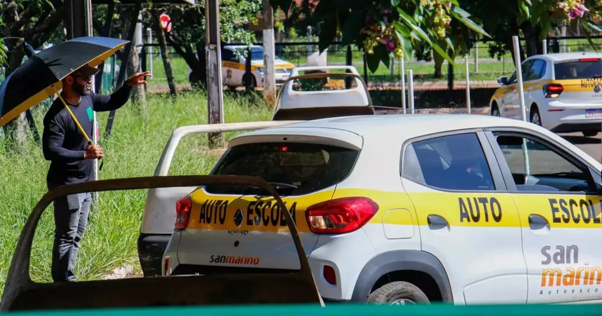 Carro de autoescola estacionado na via com examinador segurando prancheta ao lado da janela do motorista